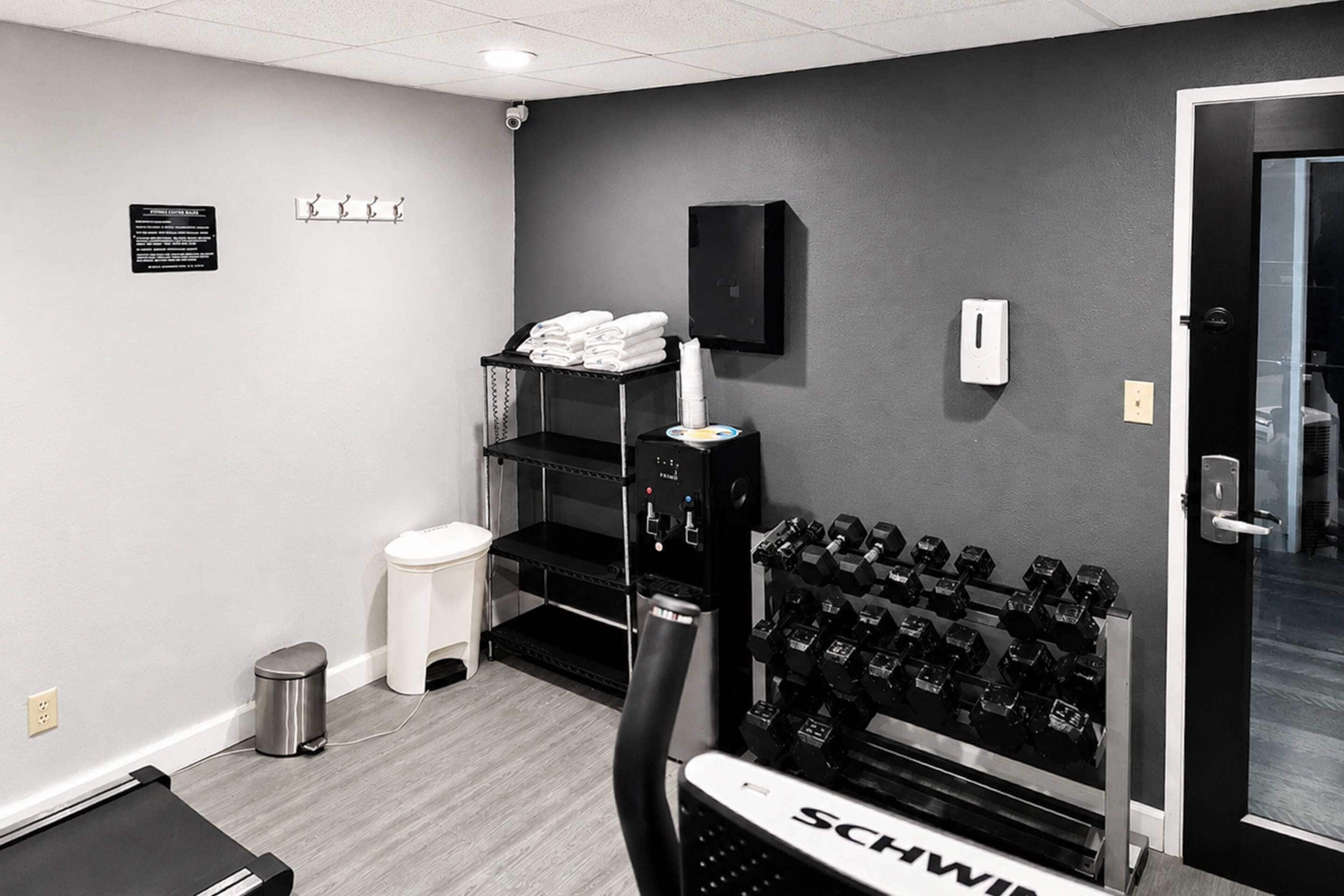 A gym with a weight bench, dumbbells, a trash can, and a towel rack.