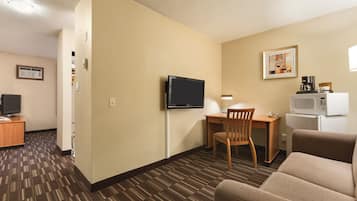 A hotel room with a flat-screen TV, a desk with a chair, a microwave, and a sofa.