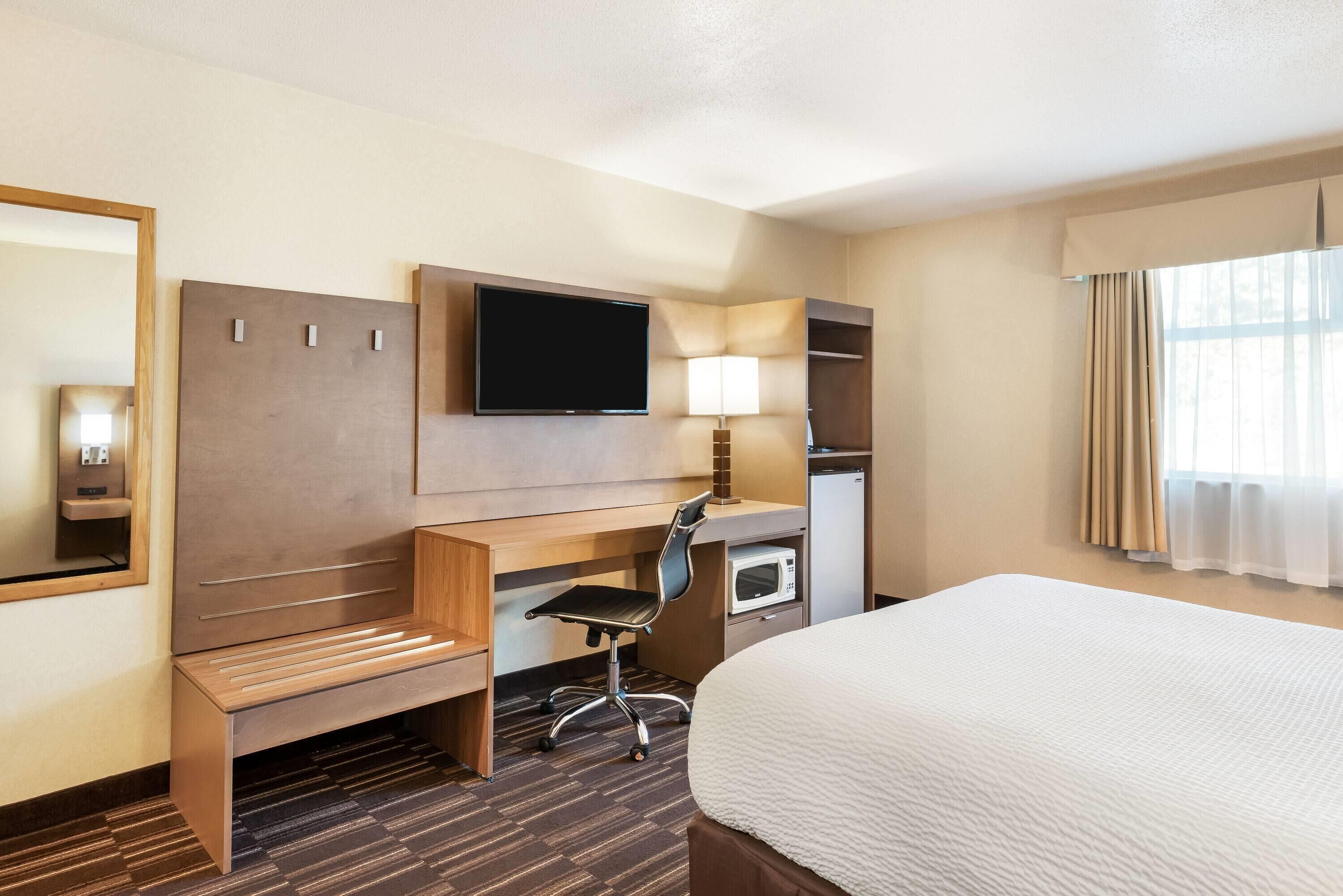 A hotel room with a bed, desk, chair, television, and a mirror.