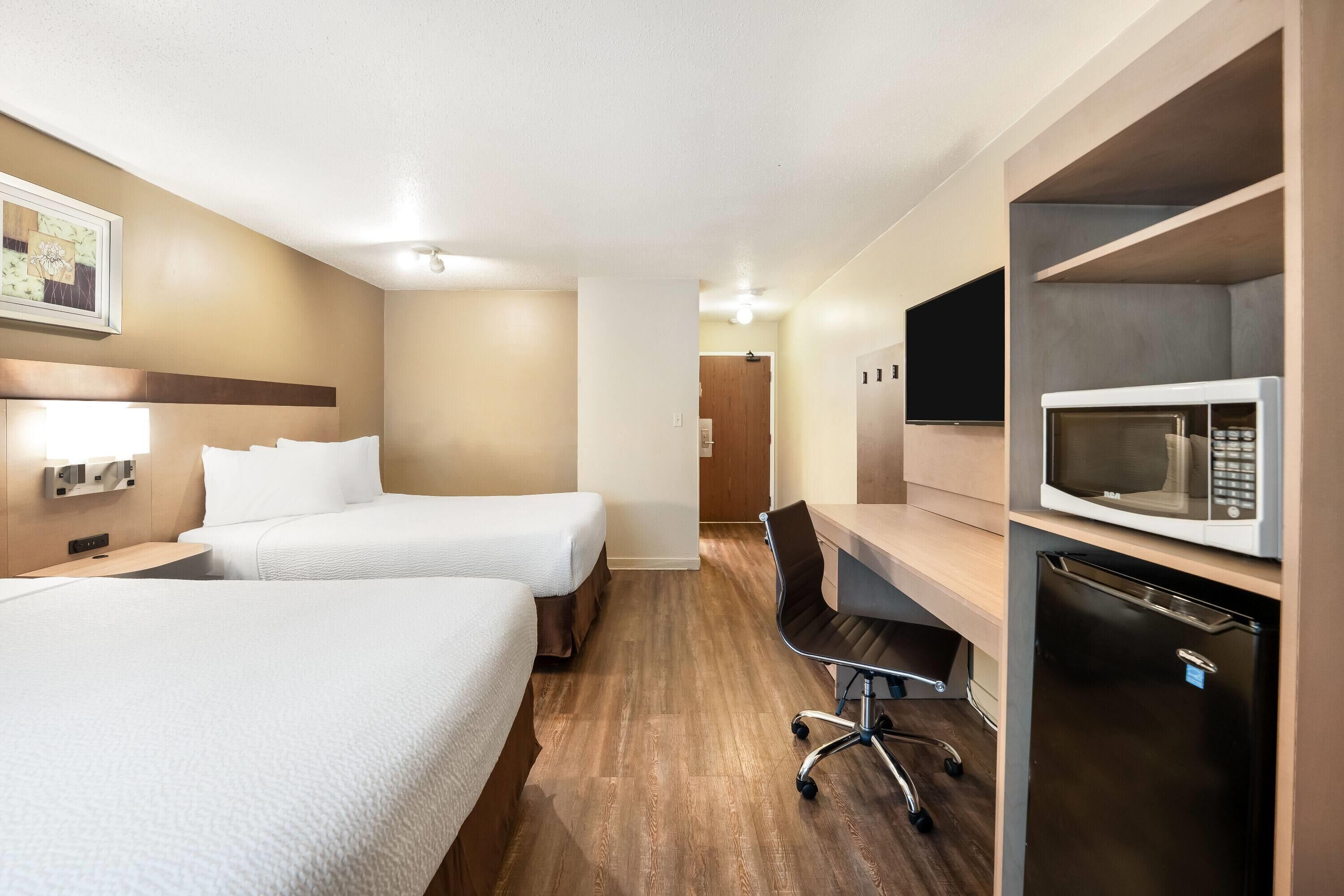 A hotel room with two beds, a desk with a chair, a microwave, and a refrigerator.
