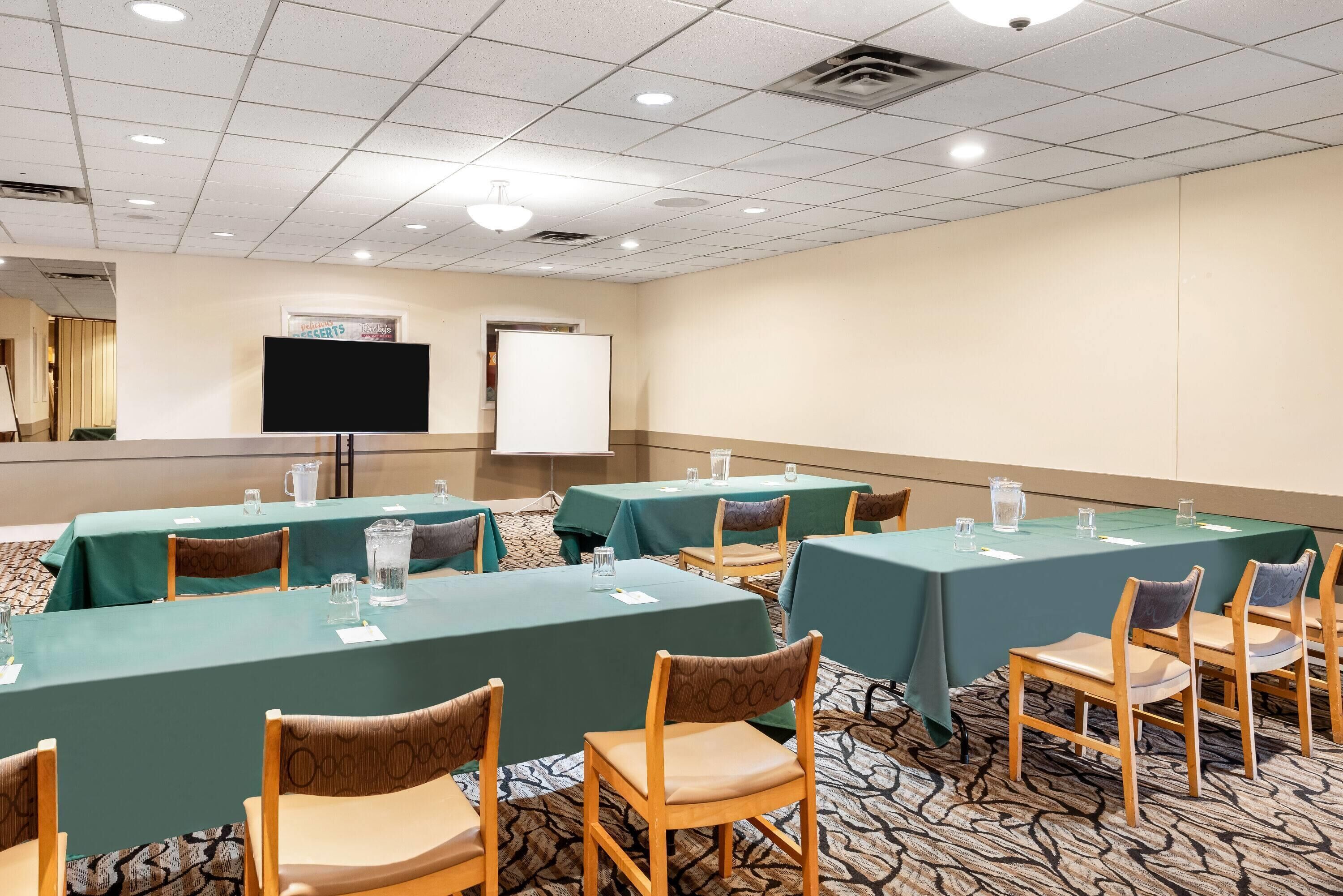 A conference room with multiple tables, chairs, a projector screen, and a whiteboard.
