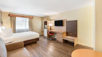 Una habitación de hotel con cama, escritorio, silla, televisor y una pequeña mesa.
