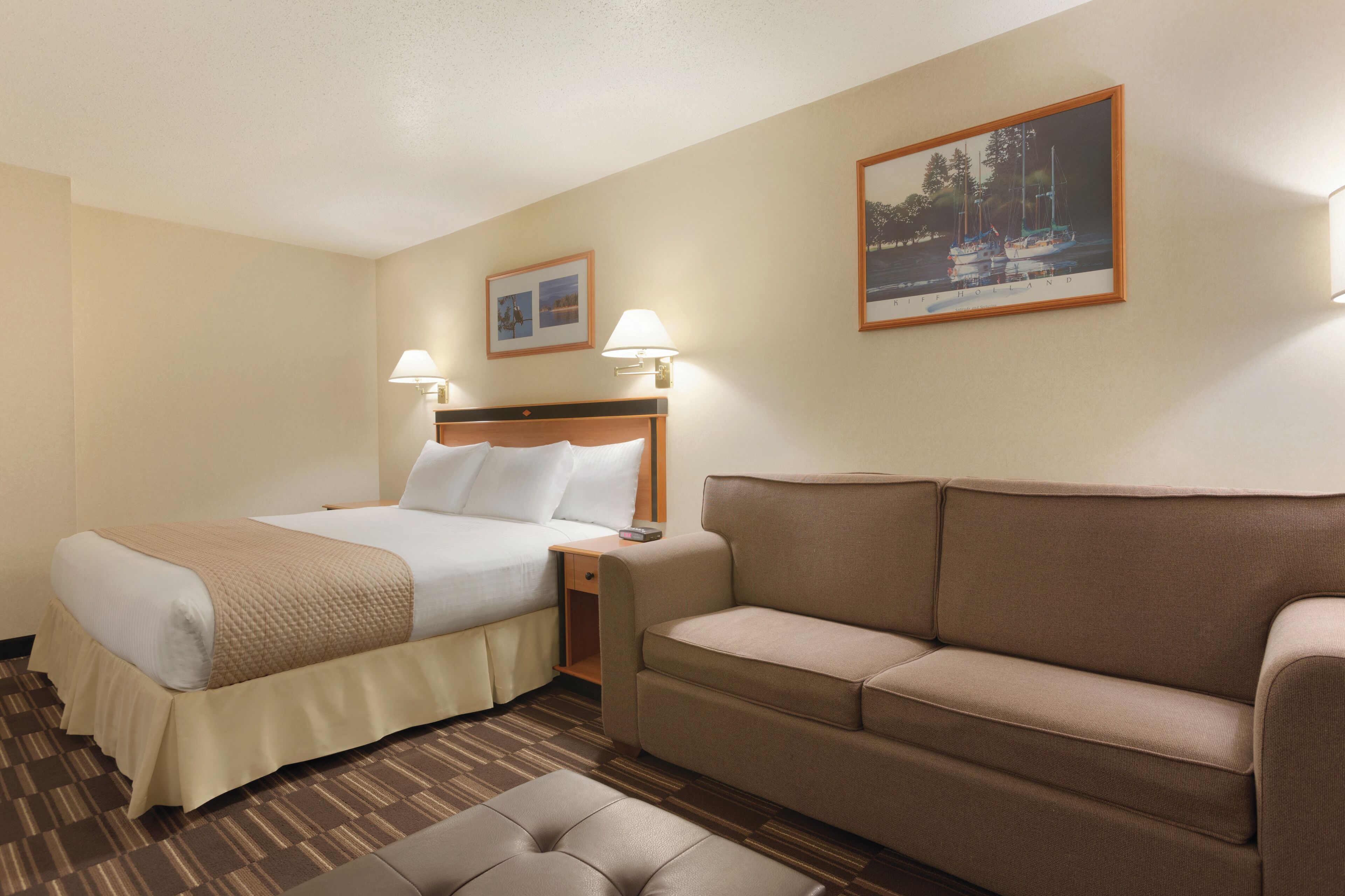 A hotel room with a bed, a sofa, a nightstand, and a lamp.