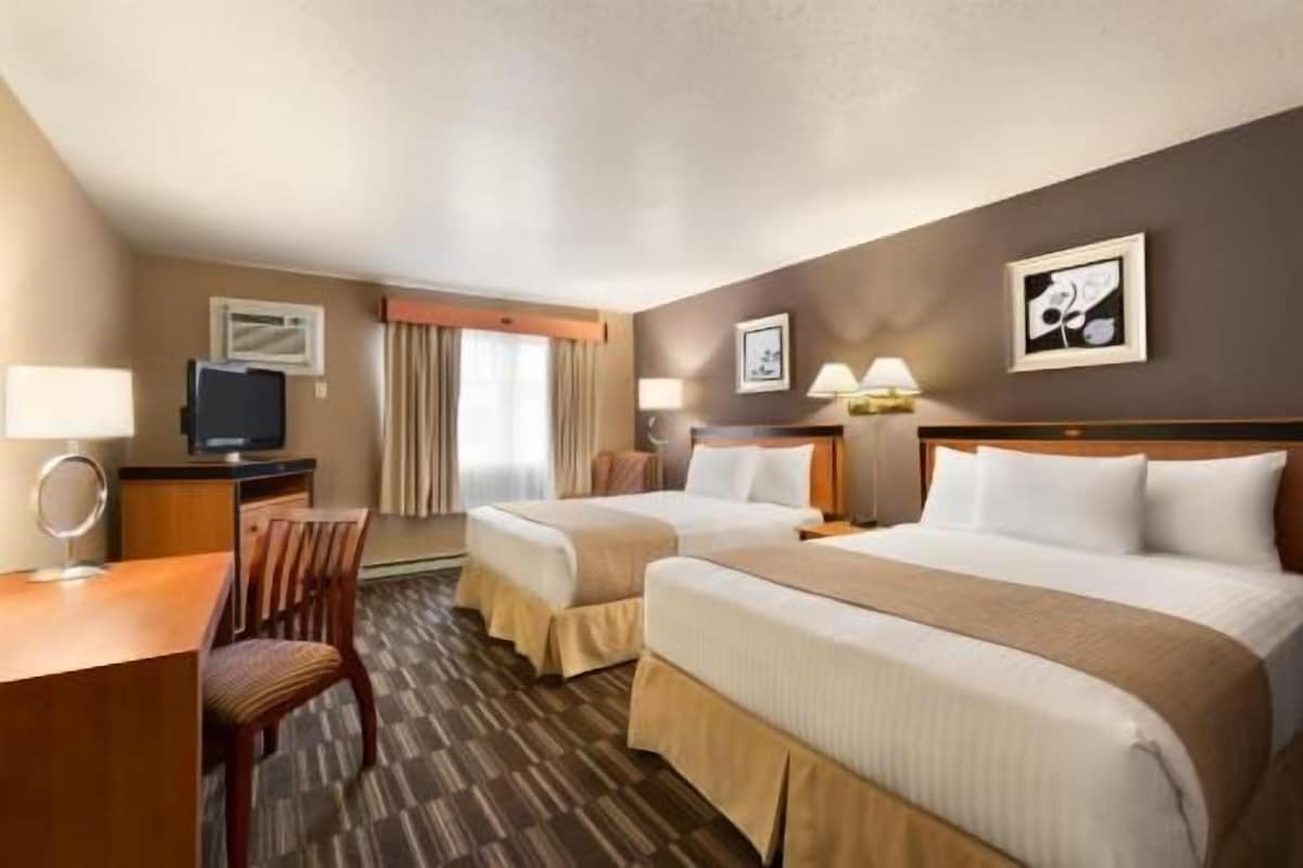 A hotel room with two beds, a desk, a chair, and a television.