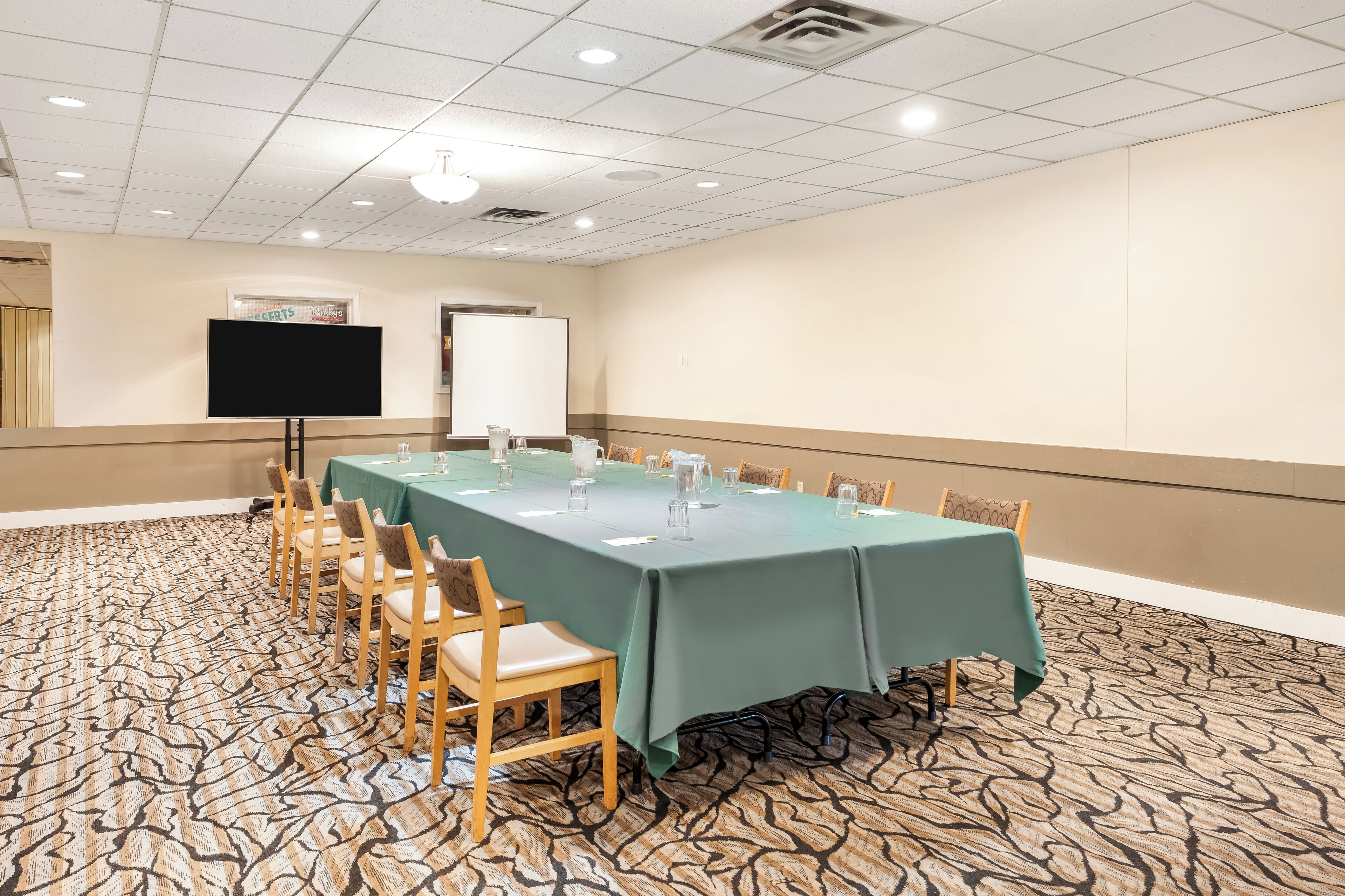 A conference room with a long table, chairs, a TV, and a whiteboard.