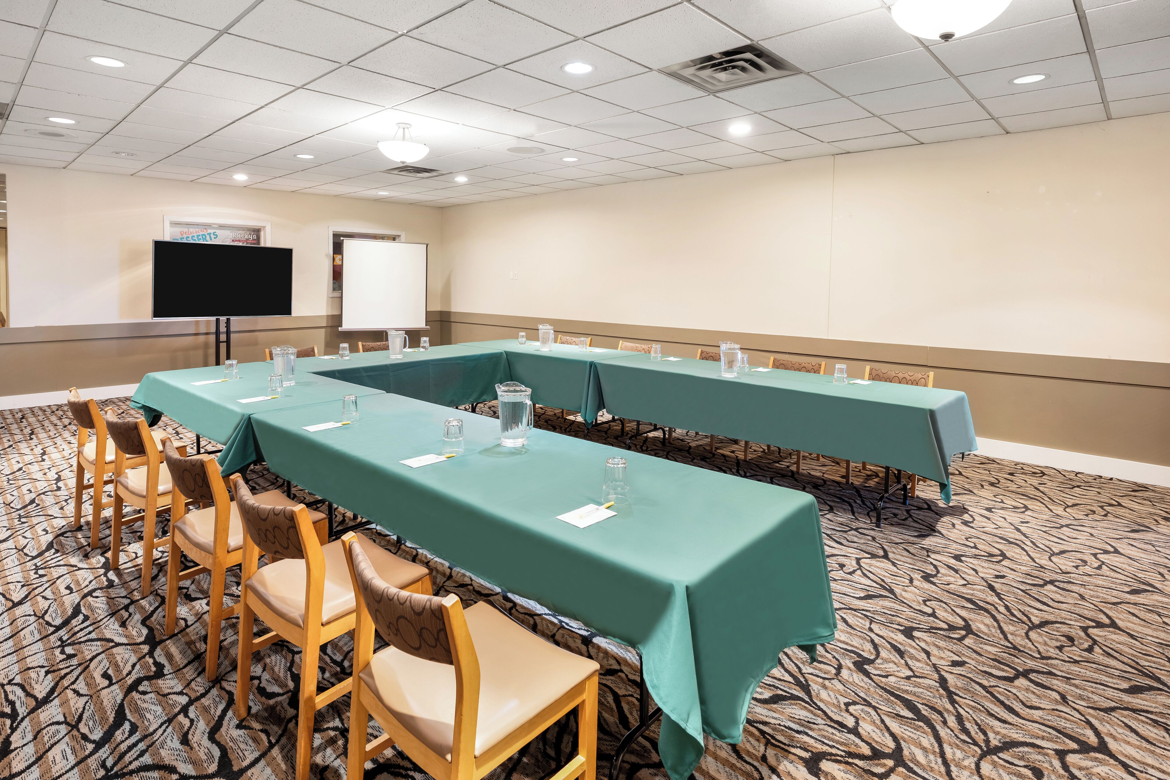 A conference room with long tables, chairs, a projector screen, and a whiteboard.