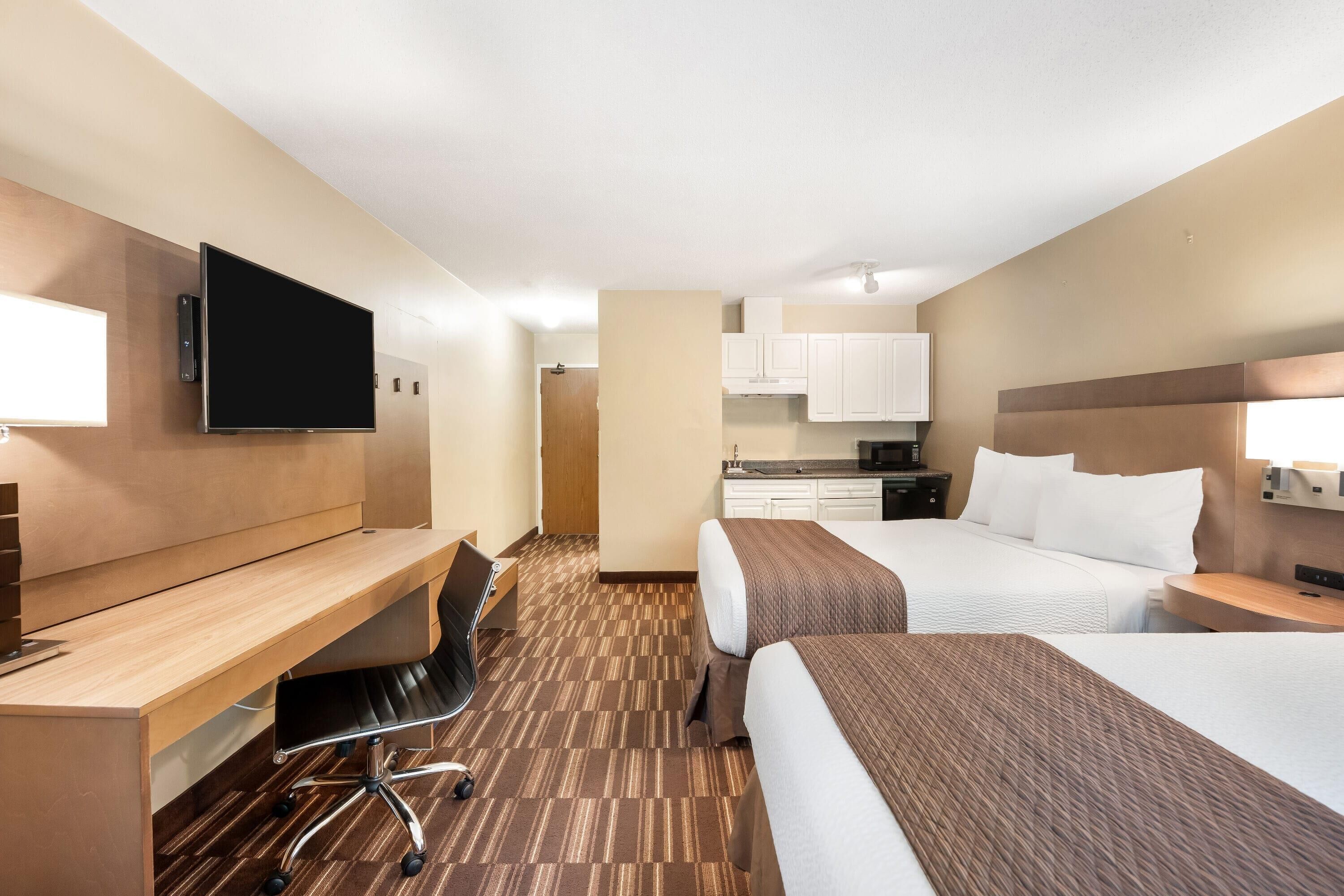 Una habitación de hotel con escritorio, dos camas, televisor, kitchenette y baño.