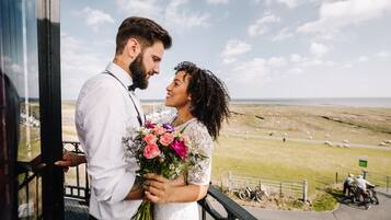 A couple embracing on a balcony with a view of a grassy field and distant horizon.