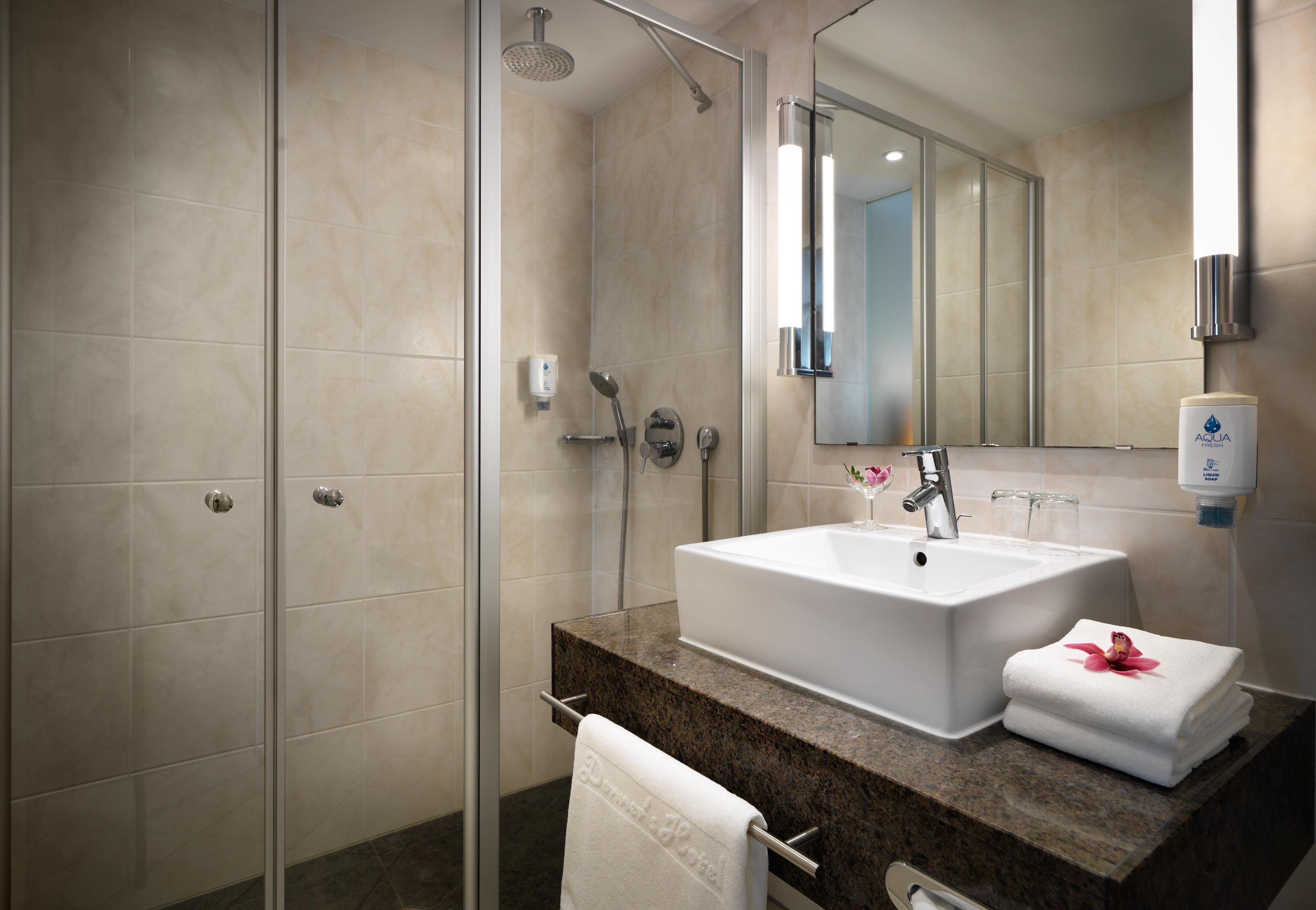 A modern bathroom with a glass shower enclosure, a white sink, and a marble countertop.