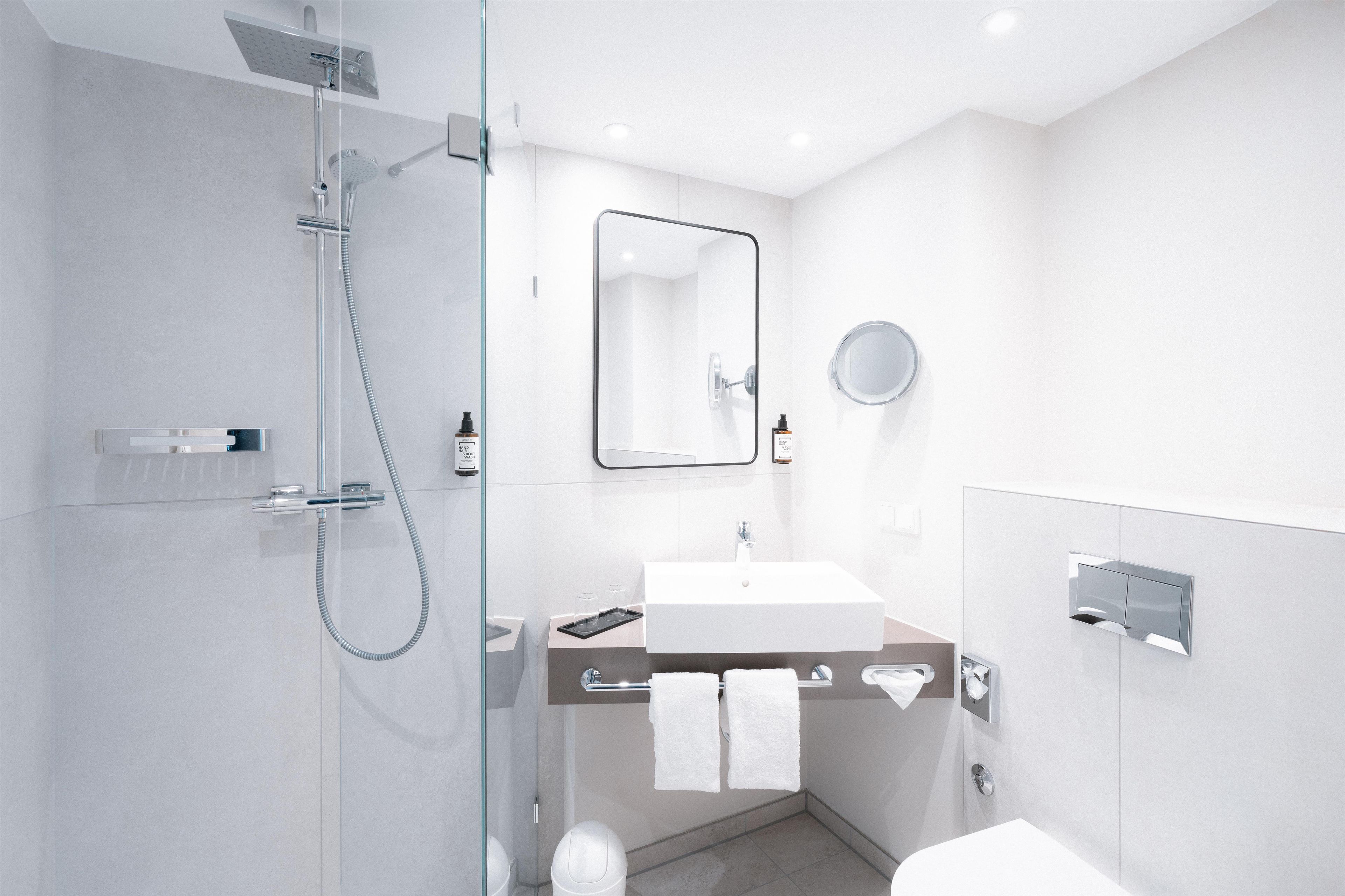 Un baño moderno con ducha envuelta en vidrio, un lavabo con espejo y un inodoro.