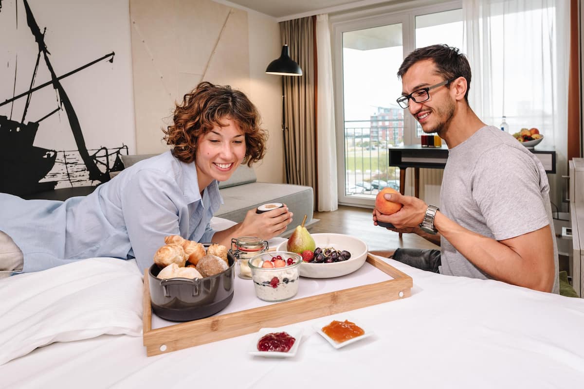 A hotel room with a bed, breakfast tray, and a view of the city.