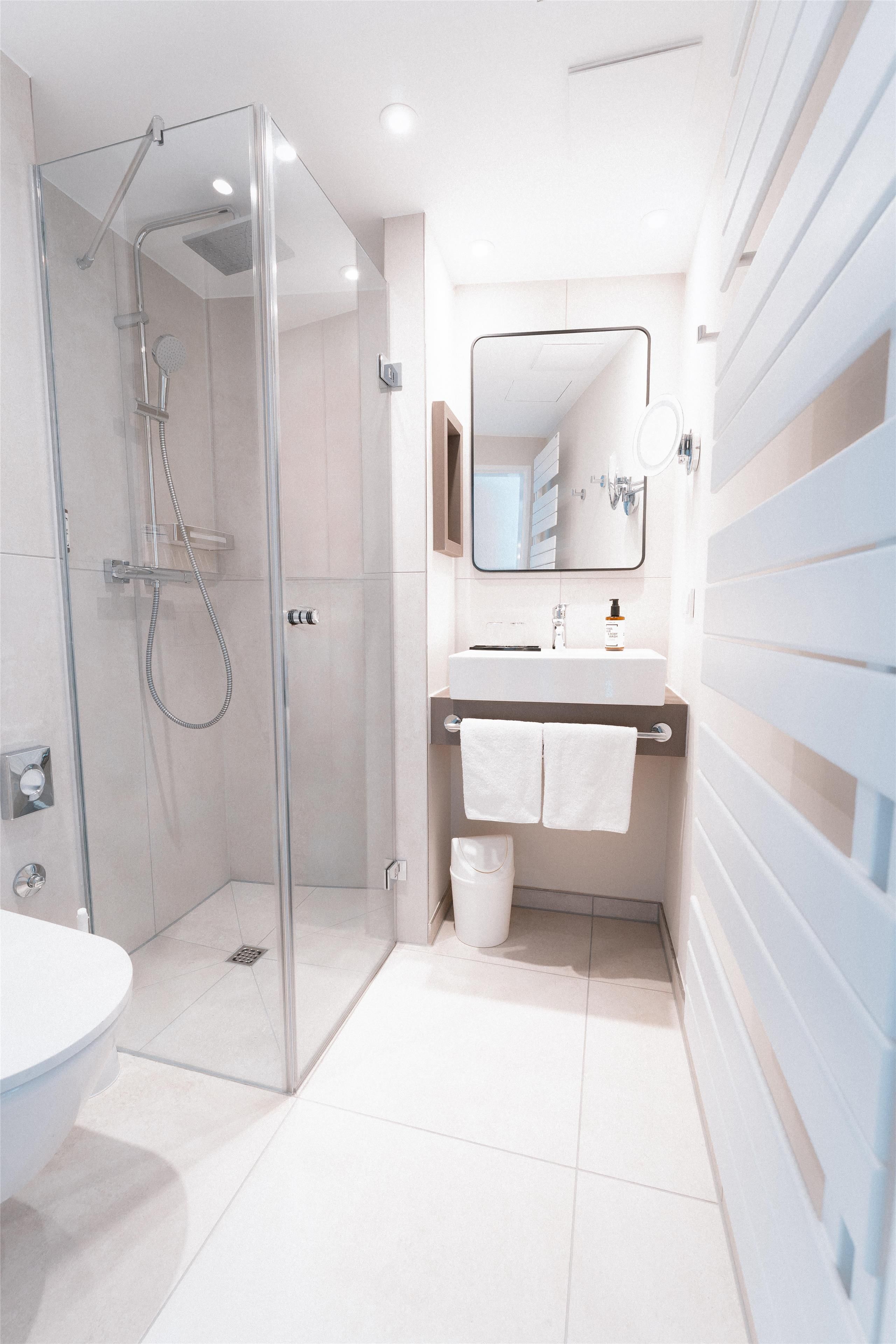 Ein modernes Badezimmer mit einer gläsernen Dusche, einem weißen Waschbecken mit Spiegel darüber und einem weißen Handtuch an einem Haken.