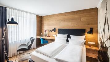 Habitación de hotel con cama, escritorio, silla y un ventanal con cortinas.