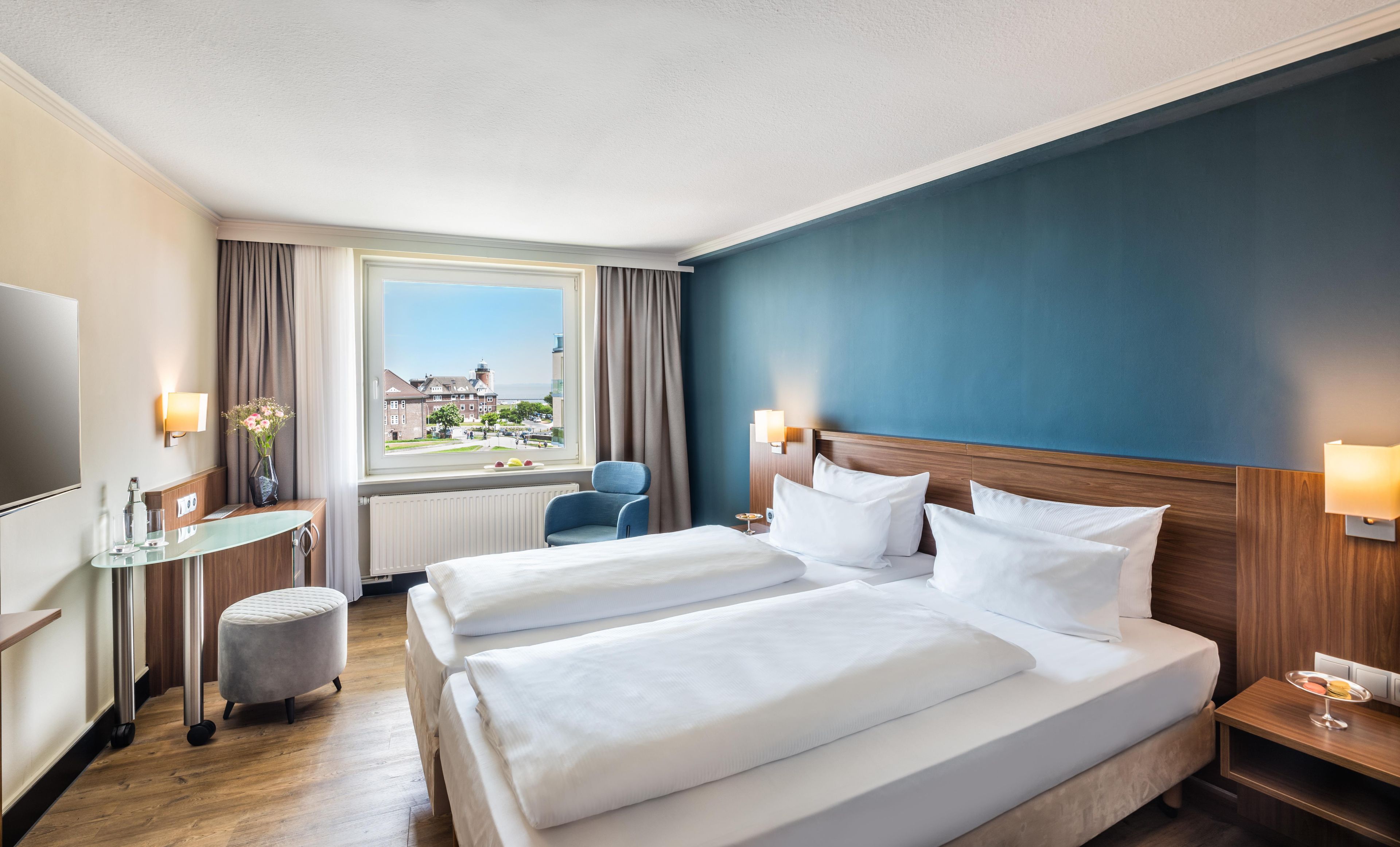 A hotel room with two beds, a desk, a chair, a TV, and a window with a view of buildings.