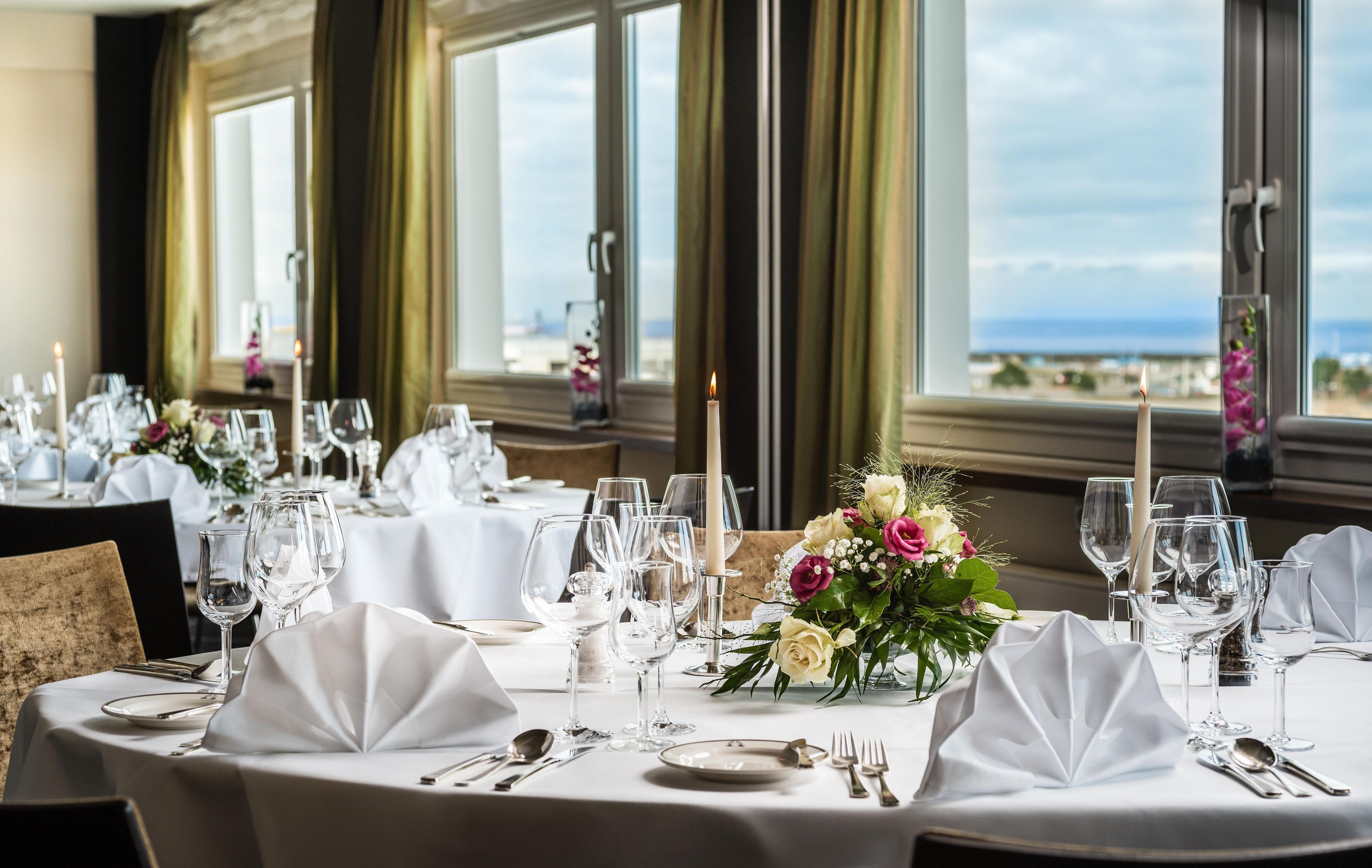 A restaurant table set with white tablecloths, candles, and a floral centerpiece.