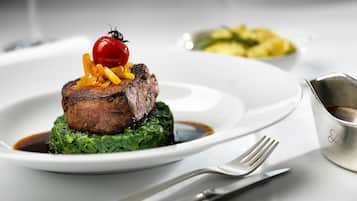Un plato con un filete, un tomate cherry y una guarnición sobre una cama de hojas verdes.