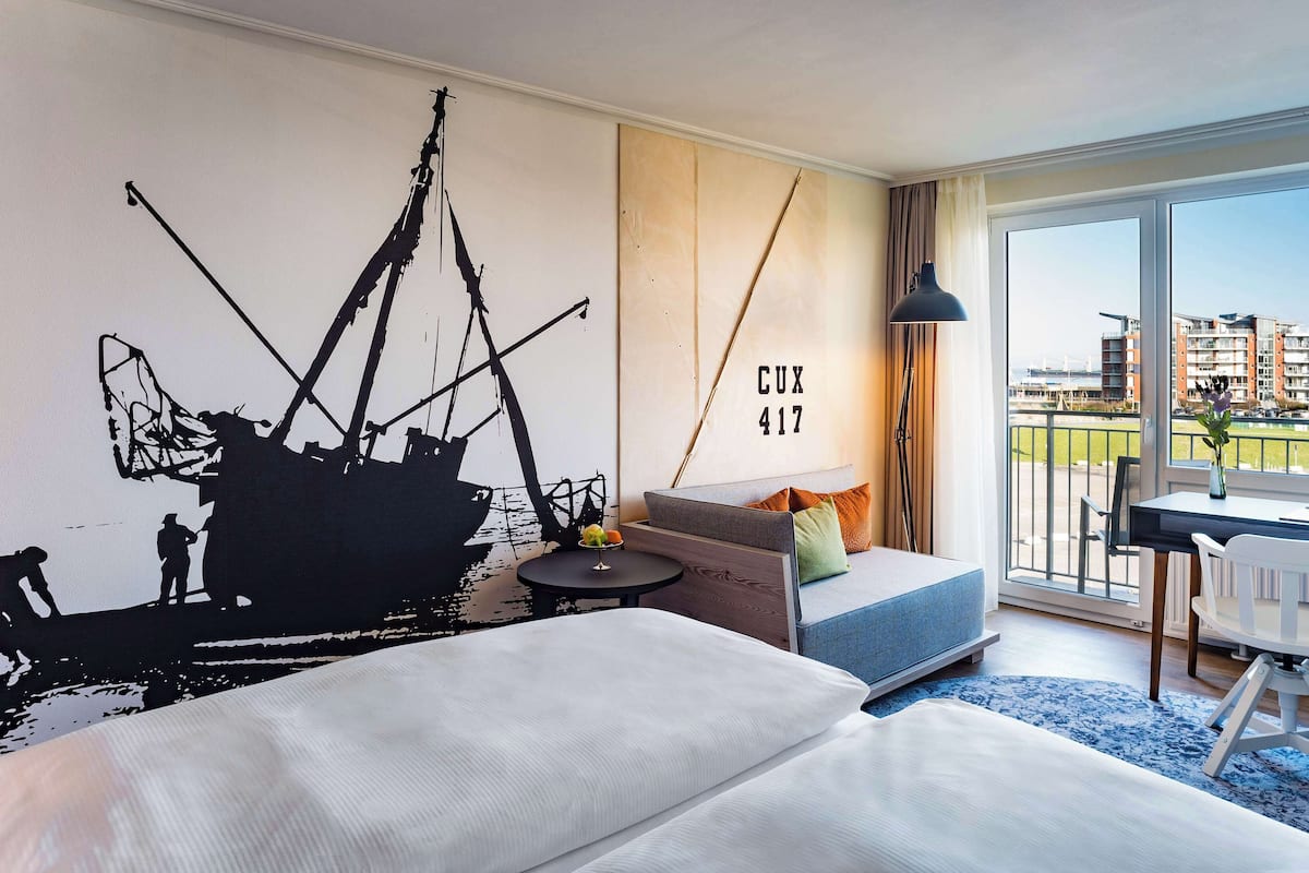 A modern hotel room with a large bed, a sofa, a desk, and a view of the city.