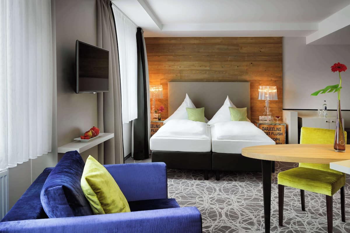 A hotel room with a bed, a TV, a sofa, a table, and a chair.