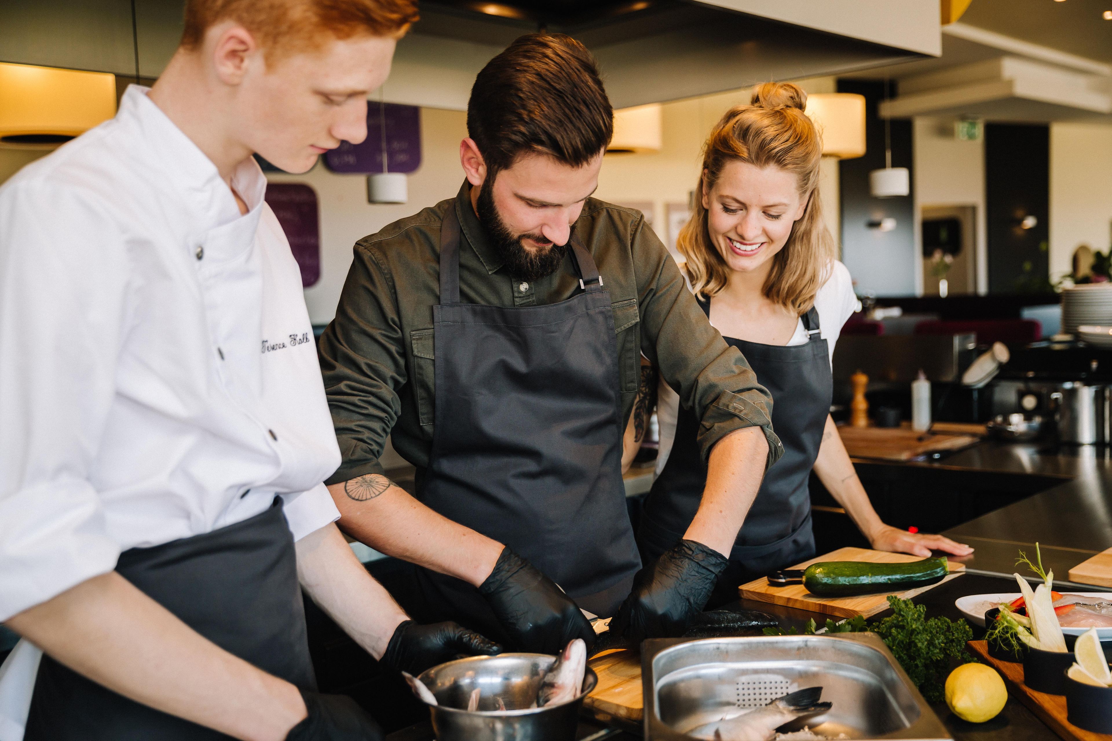 Three individuals in a kitchen setting, engaged in food preparation.