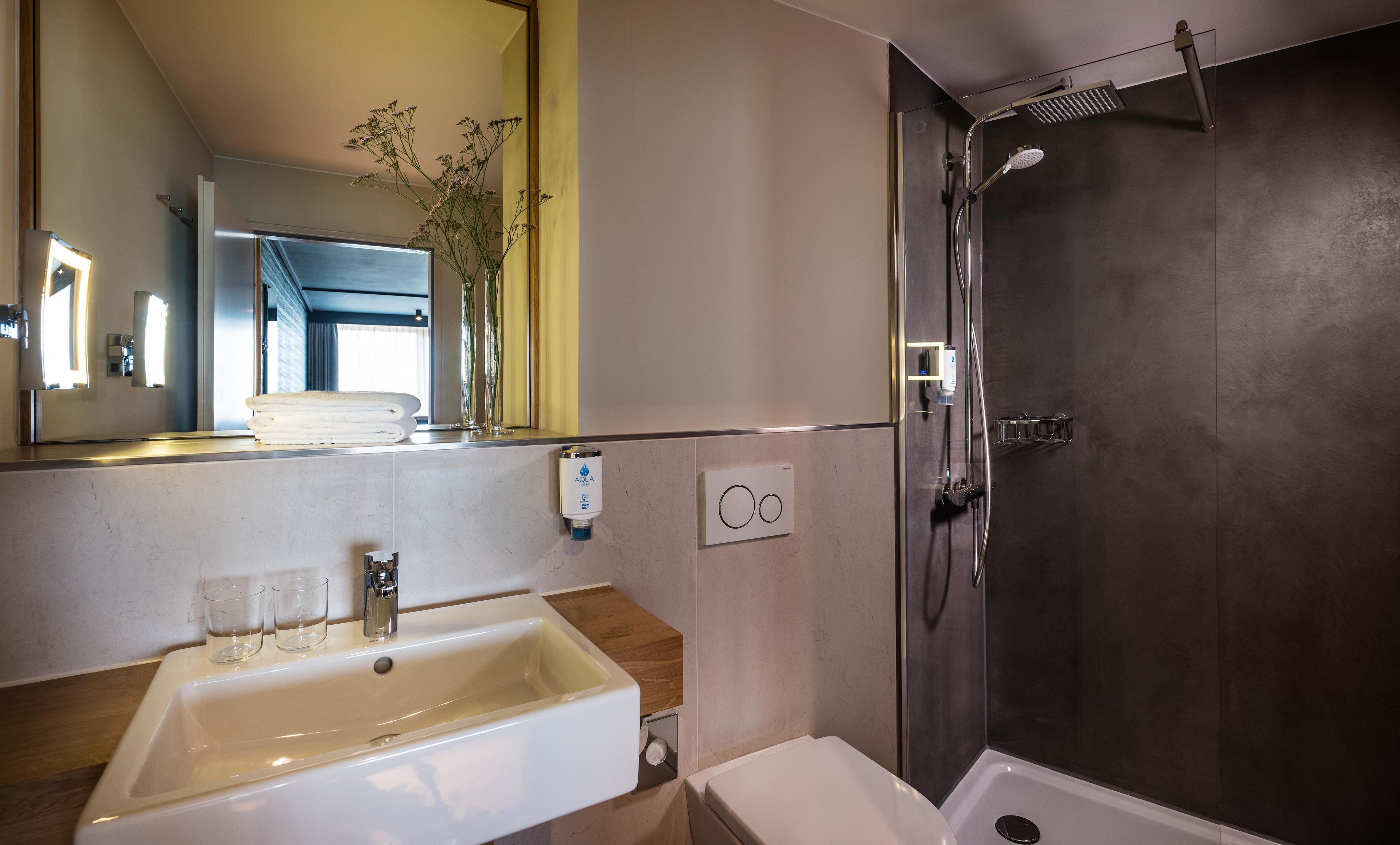 A bathroom with a sink, mirror, shower, and a towel rack.