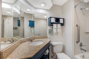 A modern bathroom with a granite countertop sink, a toilet, a shower with a grab bar, and a large mirror. - Best Western St. Louis Fairview Heights (Fairview Heights)