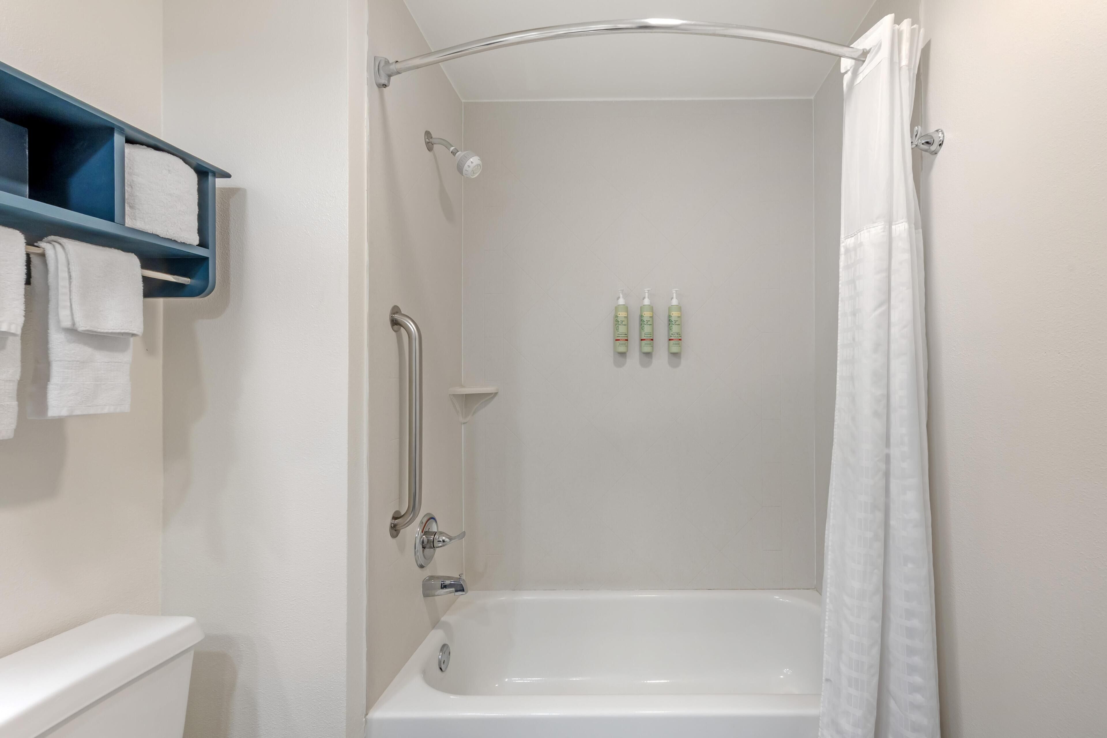 Ein Badezimmer mit einer Badewanne, einer Dusche, einem blauen Handtuchhalter und drei Flaschen an der Wand.