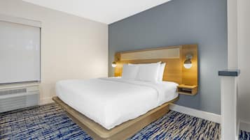 A hotel room with a bed, a headboard with wall-mounted lights, a white wall, and a blue patterned carpet.