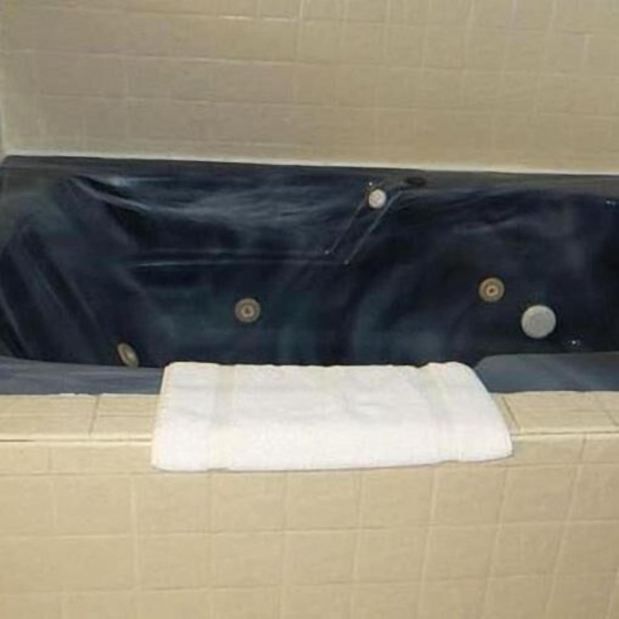 A bathtub with a dark interior, a white towel on the edge, and beige tiled walls.