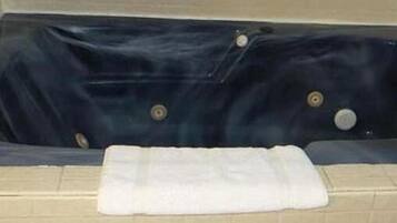A bathtub with a dark interior, a white towel on the edge, and beige tiled walls.