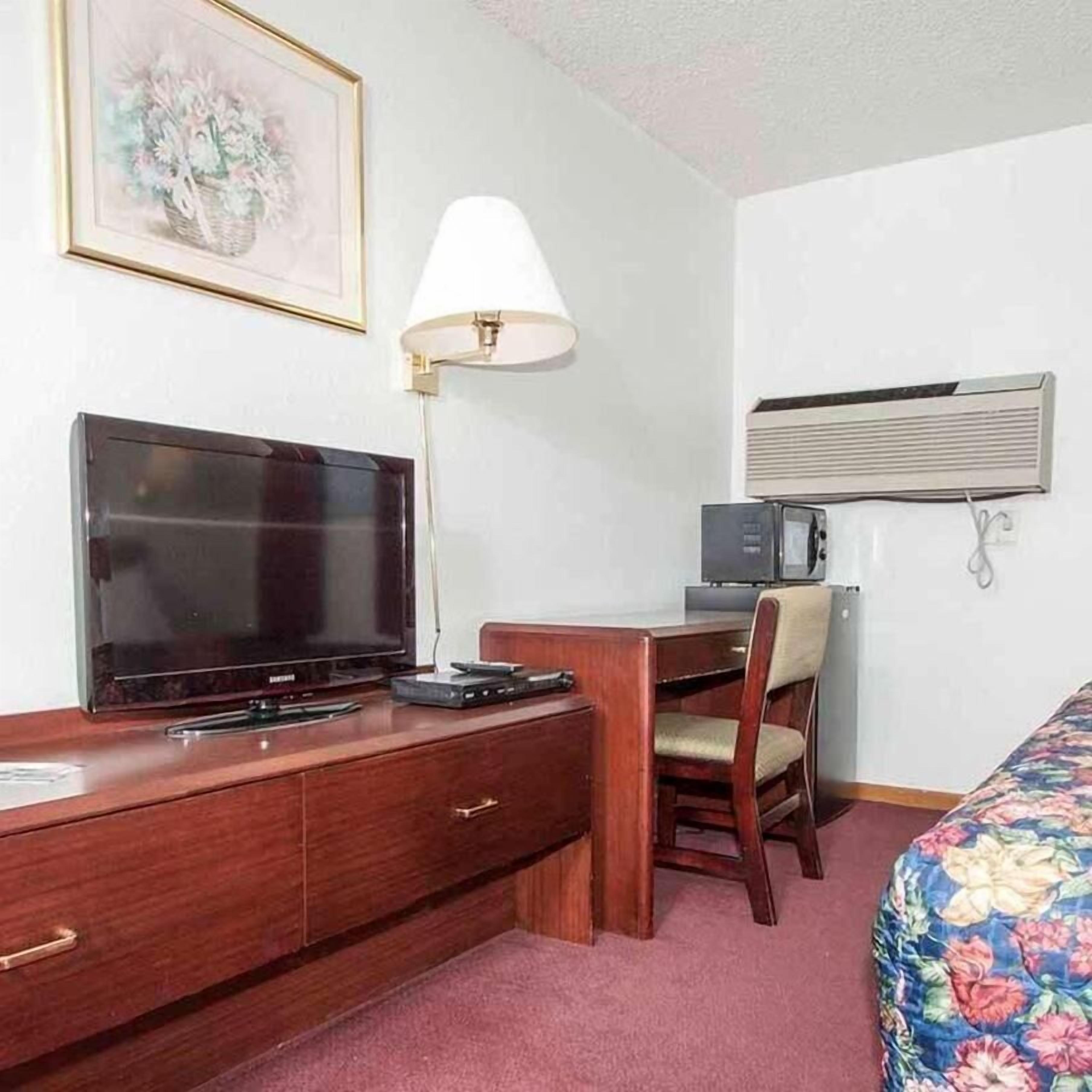 Una habitación de hotel con una cama, un escritorio con televisor, una lámpara y un microondas.