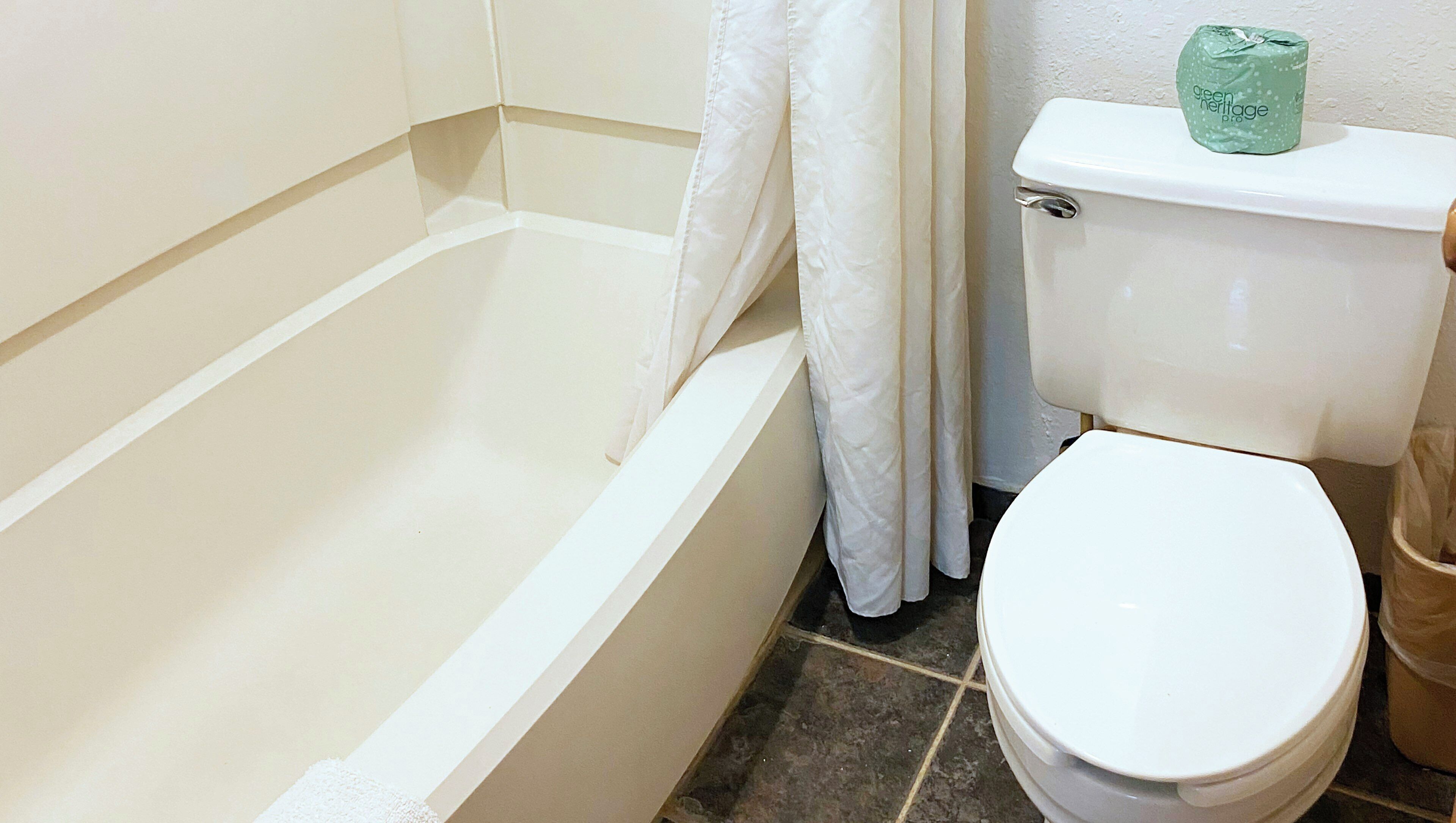 A bathroom with a bathtub, toilet, and a green bottle on the toilet tank.