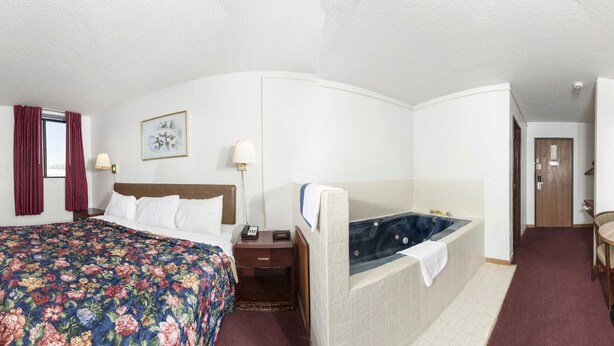 Ein Hotelzimmer mit Bett, einer Sitzecke mit Tisch und Stühlen, einem Fernseher und einem Badezimmer mit Badewanne.