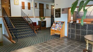 A hotel lobby with a staircase, a reception desk, a coffee station, and a display of magazines.