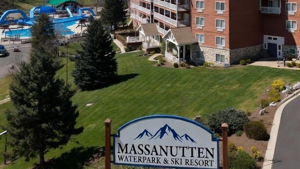 Um hotel com uma placa indicando 'Massanuten Waterpark & Ski Resort', um edifício com fachada vermelha e uma área de parque aquático com um escorrega verde.