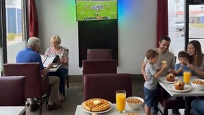 Espaço de refeições familiar com televisão de tela plana, pratos de waffle e suco.