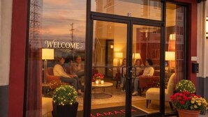 Entrada de hotel com um letreiro 'WELCOME', área de recepção com assentos e tapete de entrada com a inscrição 'RAMADA BY WYNDHAM'.