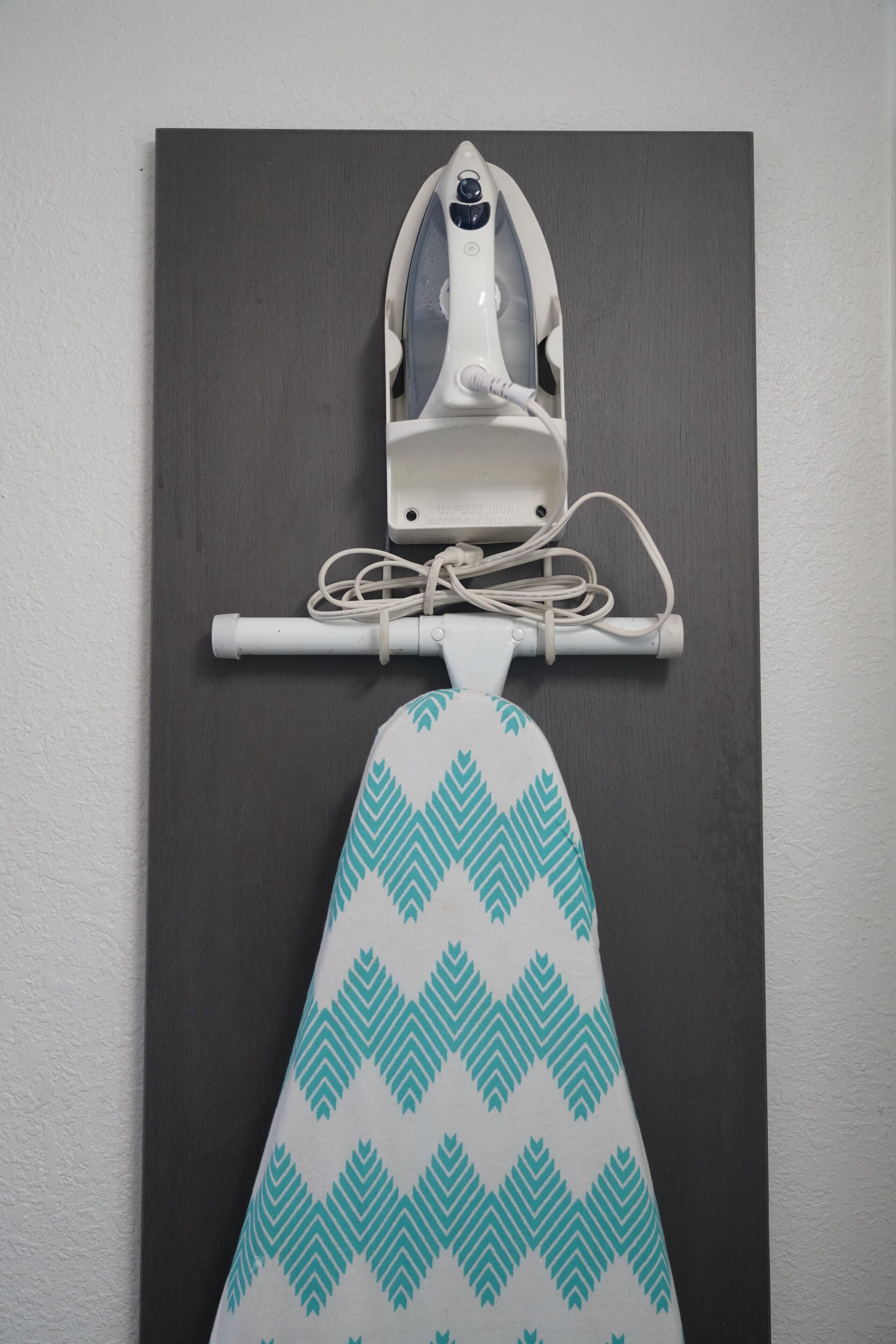 A wall-mounted ironing board with an iron and a patterned towel.
