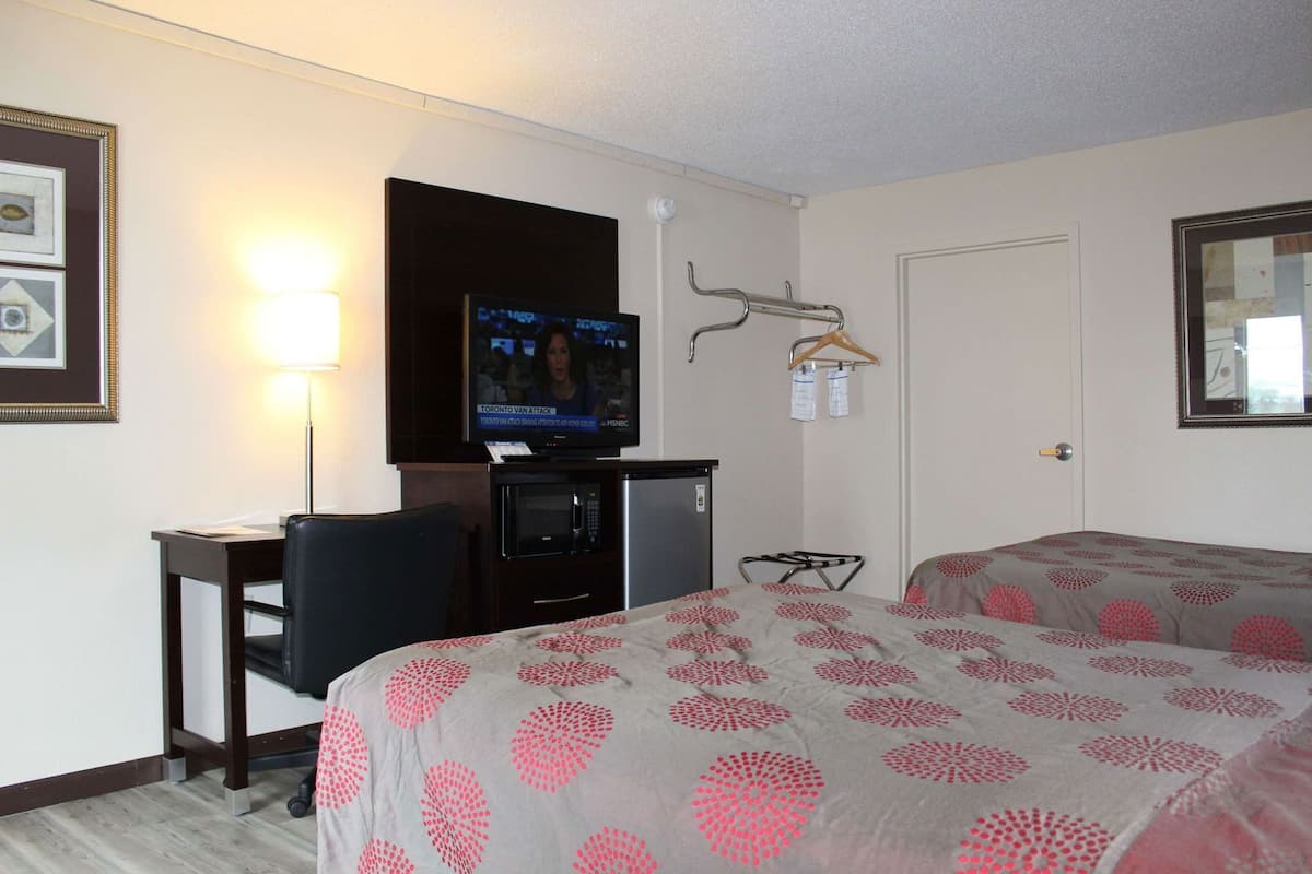 A hotel room with a bed, a desk with a TV, a microwave, a chair, and a coat rack.