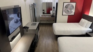 Quarto de hotel com televisão, escrivaninha, duas camas, espelho e quadro emoldurado na parede.