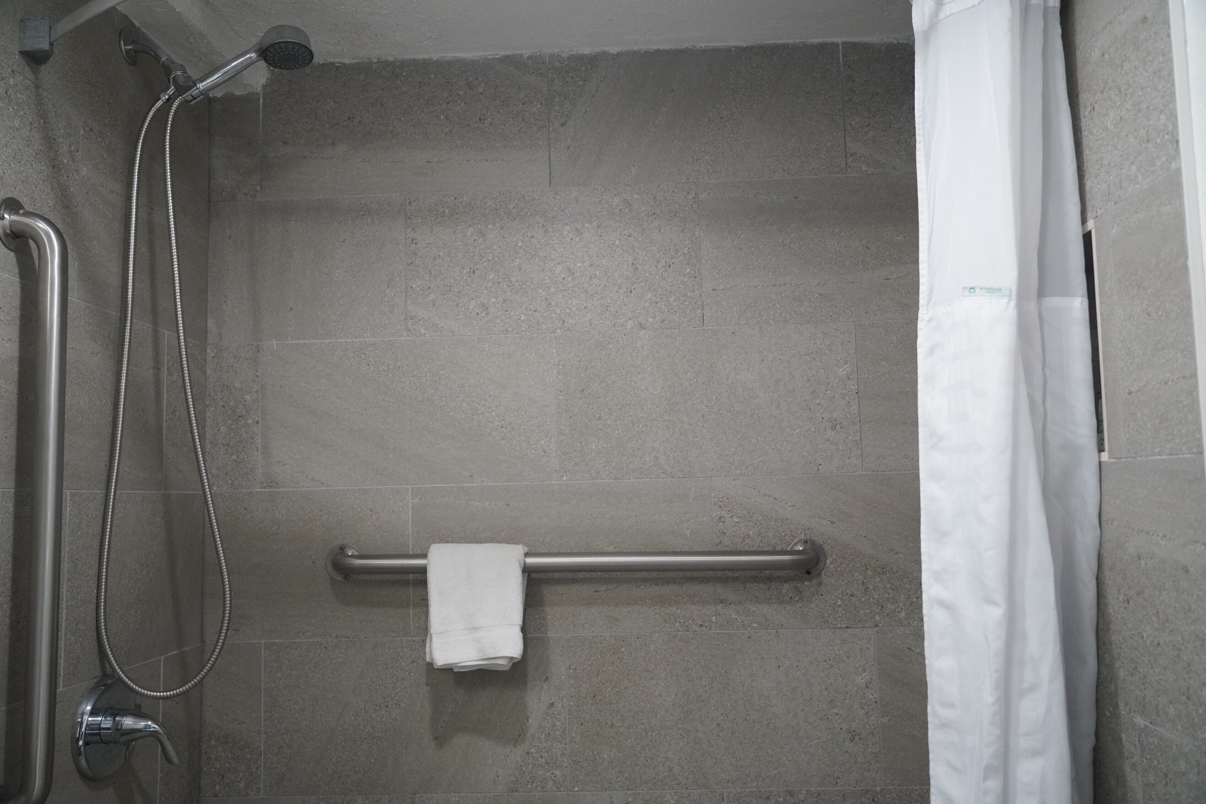 A shower area with a grab bar, a towel rack, and a showerhead.