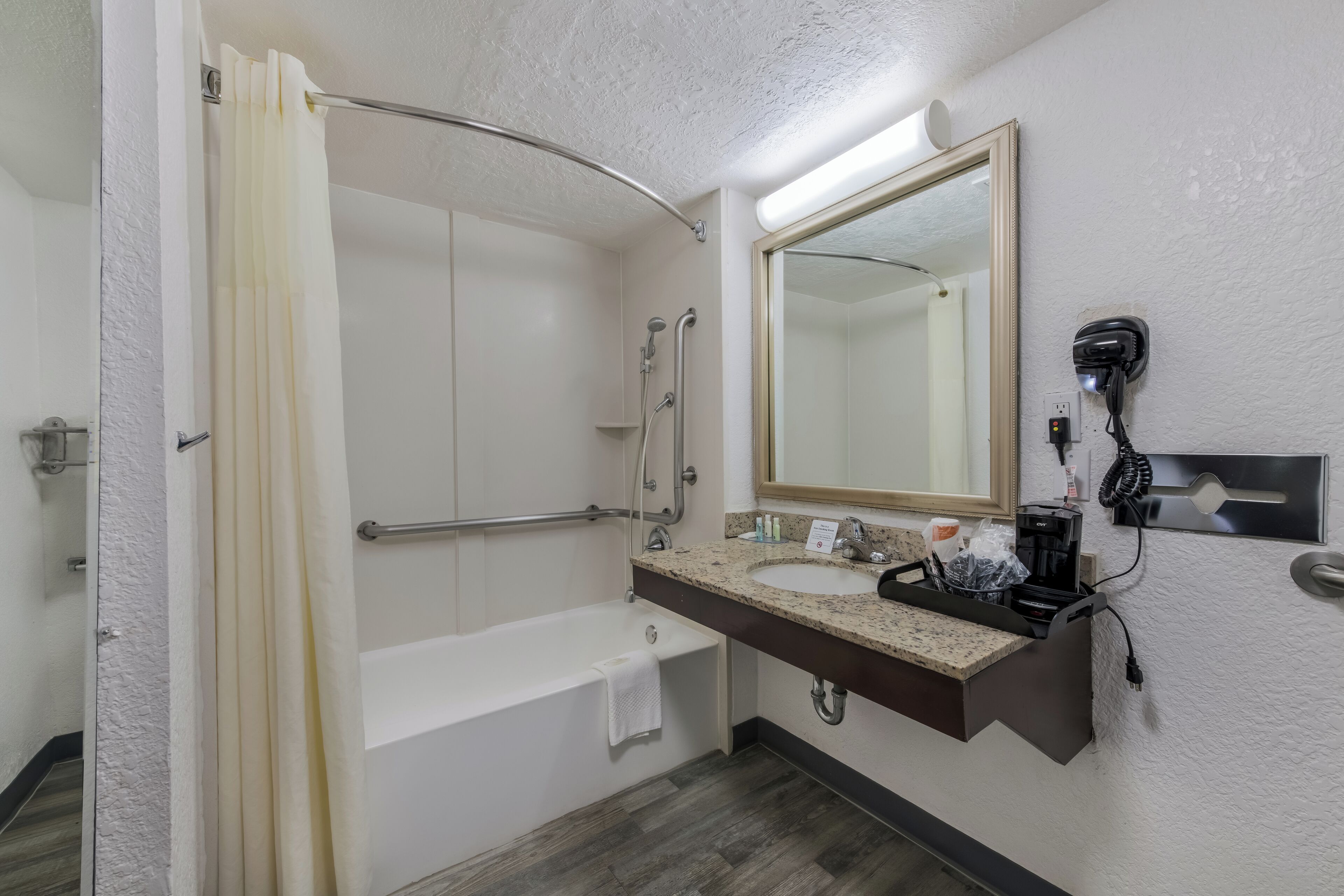 A bathroom with a bathtub, a shower, a sink with a mirror, and a hairdryer mounted on the wall.
