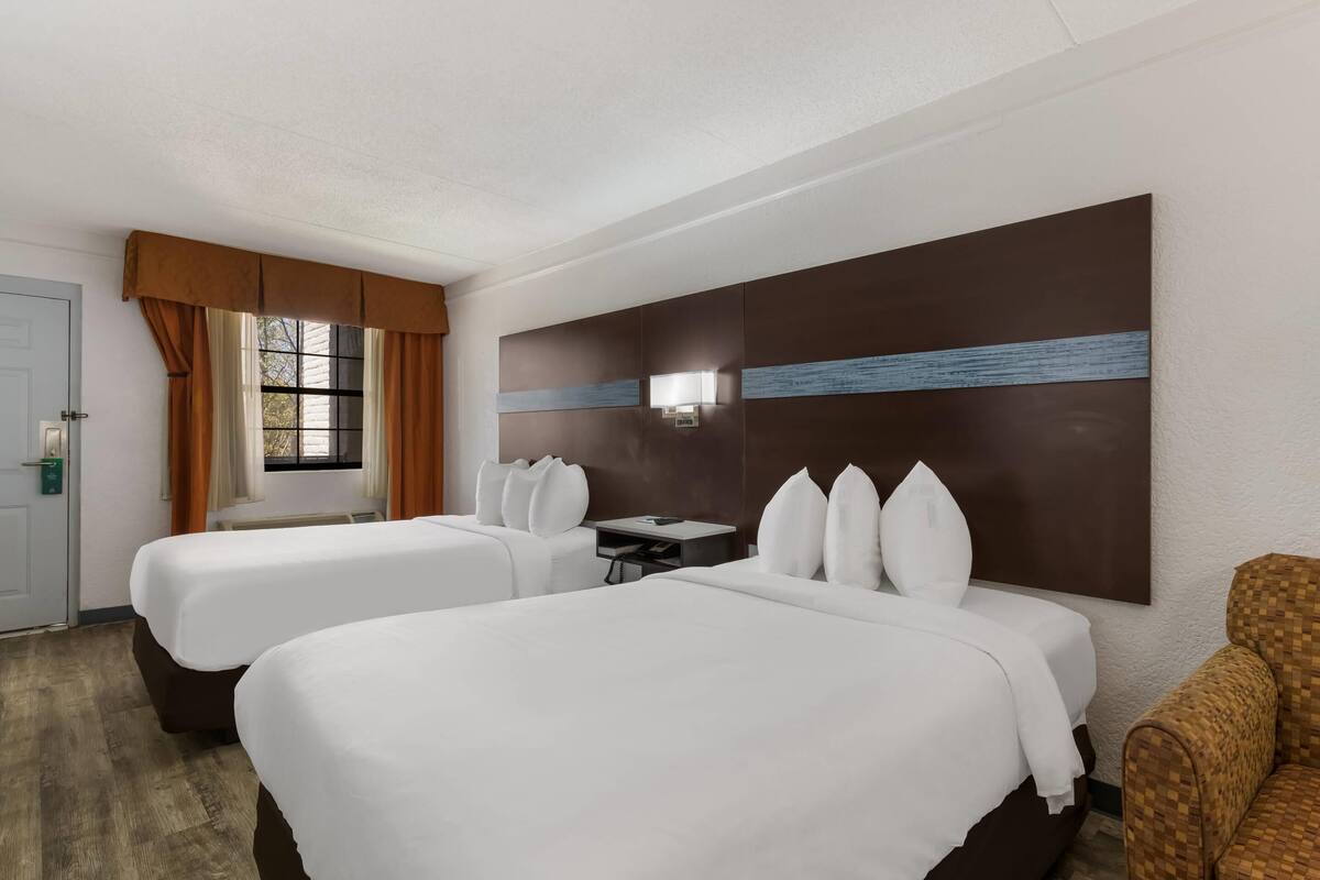 Ein Hotelzimmer mit zwei Betten, einem Schreibtisch, einem Stuhl und einem großen, an der Wand befestigten Fernseher.