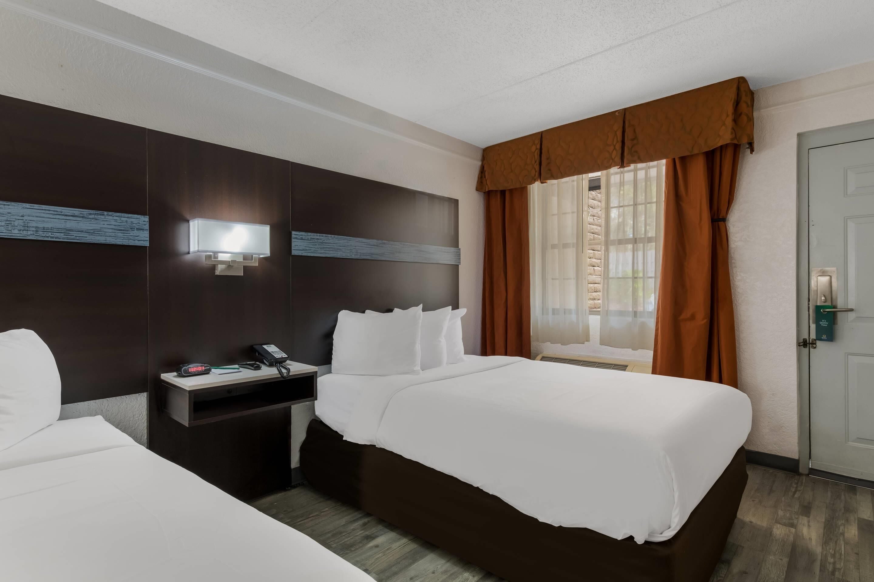 A hotel room with a large bed, a bedside table with a phone and a lamp, and a window with curtains.