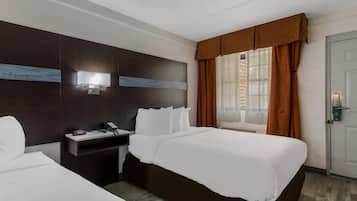 A hotel room with a large bed, a bedside table with a phone and a lamp, and a window with curtains.