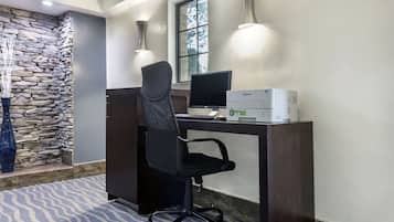 Oficina de hotel con escritorio, computadora e impresora. Se observa una pared de piedra y una ventana con luz natural.