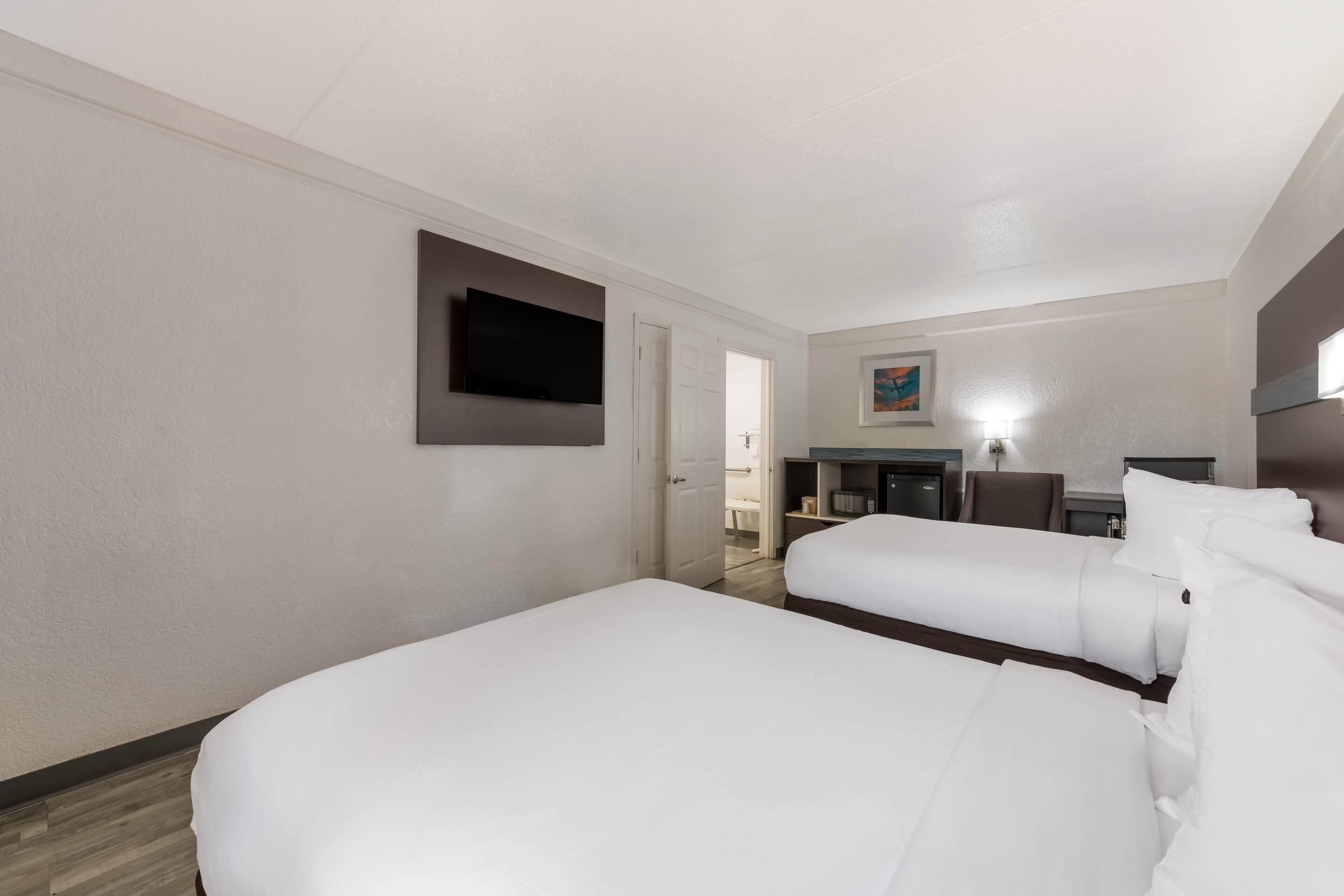 Hotellihuone, jossa on kaksi sänkyä, seinälle asennettu taulutelevisio, työpöyt ä tuolilla ja taulu seinällä.