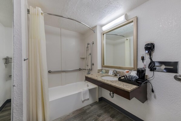 Un baño con ducha, bañera, lavamanos con espejo y secador de pelo montado en la pared.