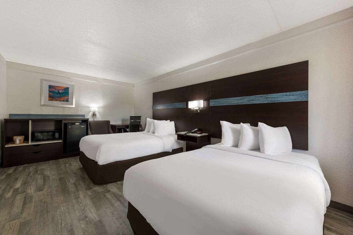 Ein Hotelzimmer mit zwei Betten, einem Schreibtisch, einer Mikrowelle, einem Kühlschrank und einem Bild an der Wand.