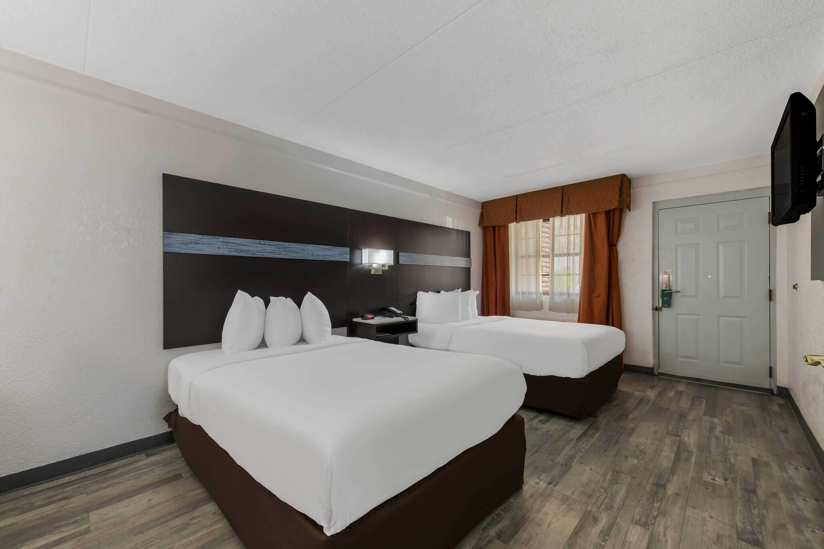 A hotel room with two beds, a flat-screen TV, a desk, and a window with curtains.