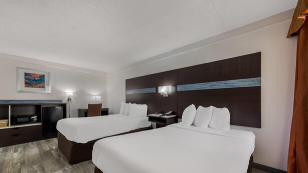 Una habitación de hotel con dos camas, un escritorio, un televisor y un cuadro en la pared.